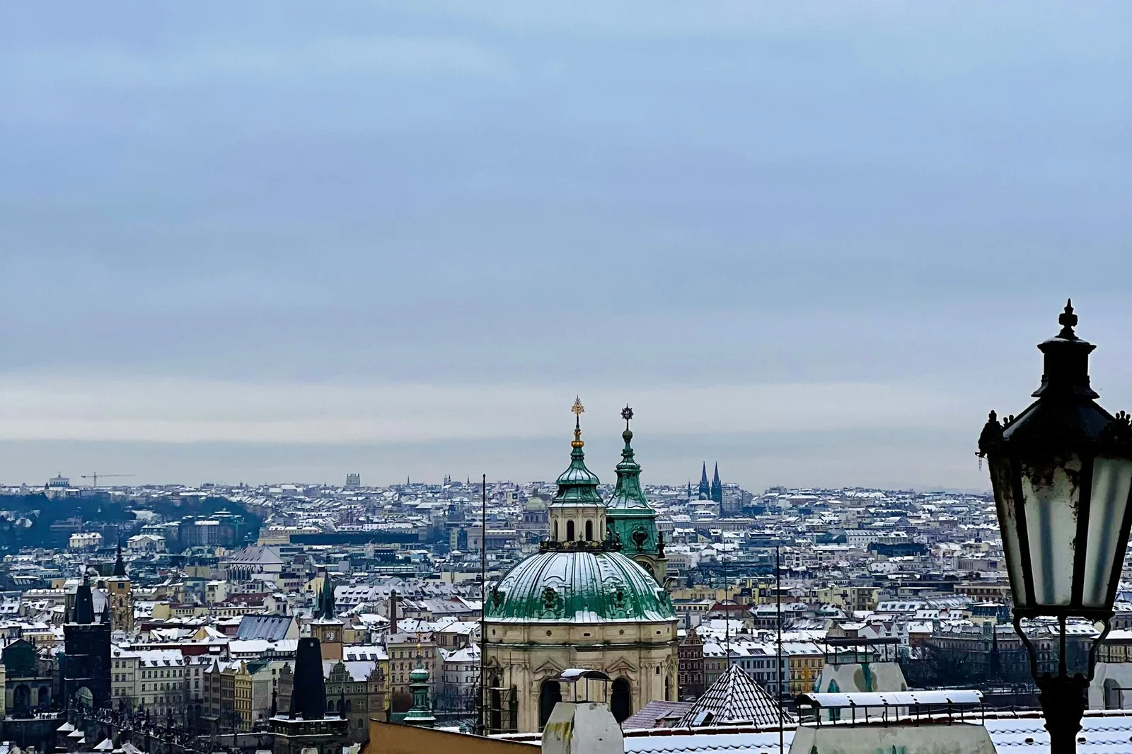 Snow-covered red rooftops of Prague with the green dome of St. Nicholas Church